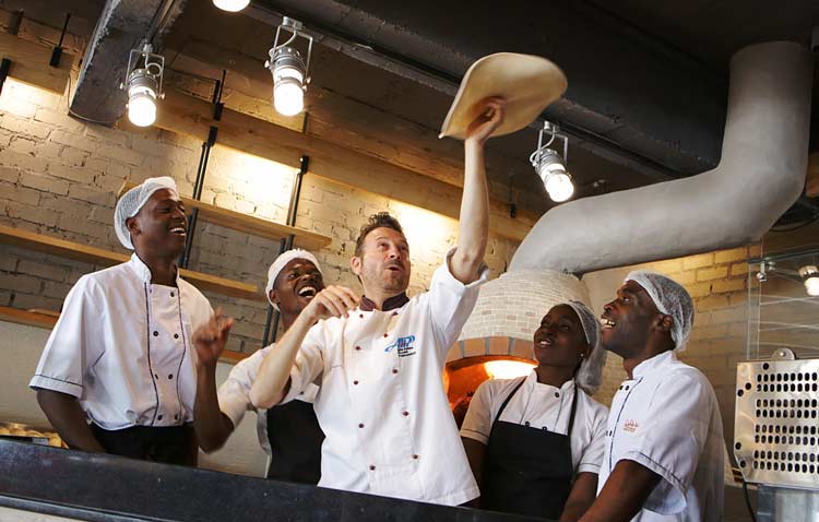 Akrobatischer Pizzabäcker und Studenten während eines Pizzakurses.